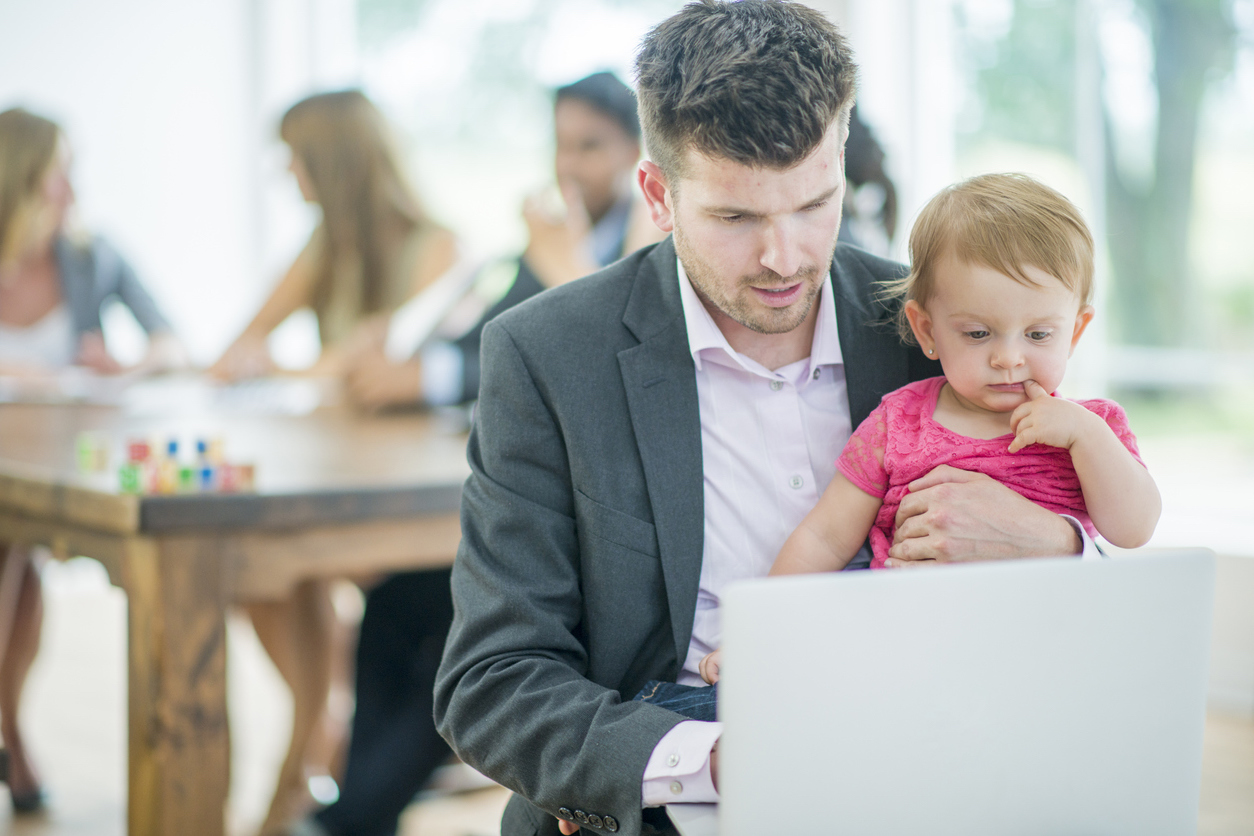 man holding his infant daughter while working on laptop
