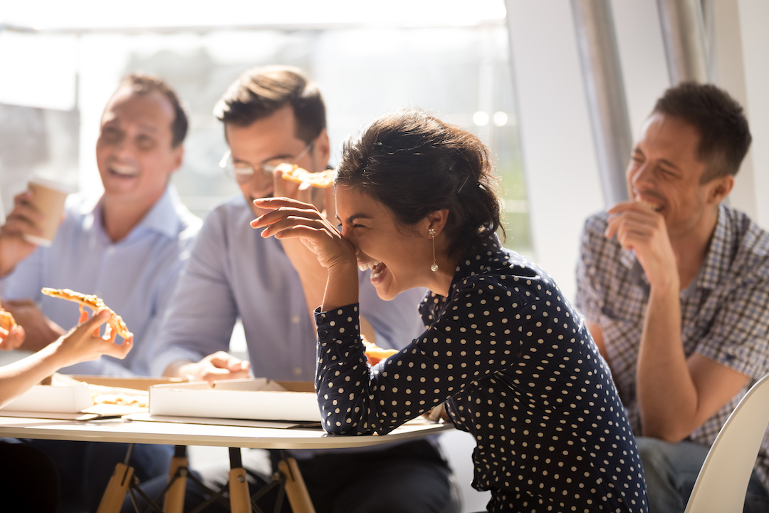 woman laughing at funny joke eating pizza with diverse coworkers in office